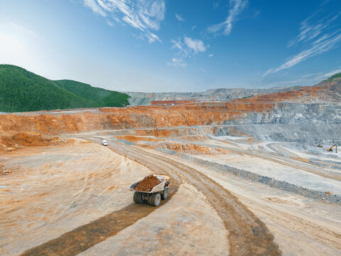 Aerial top view Mining dump truck hauling ore on winding dirt road in open pit mine