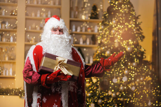 Happy Santa Claus or Father Frost with Christmas gift standing on background decorated room with festive tree. Concept of Russian New Year's winter holidays celebration card