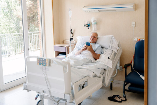 Senior male patient relaxing in hospital bed using smartphone