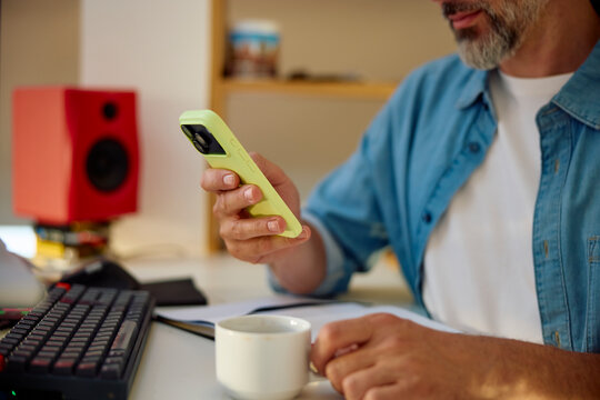 Man sits in the home office, drinking coffee and using his phone