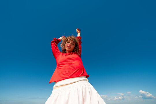 Woman posing with raised arms against blue sky