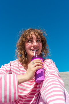 Smiling woman drinking from purple tumbler under blue sky