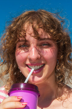 Smiling woman drinking from purple tumbler in sunlight