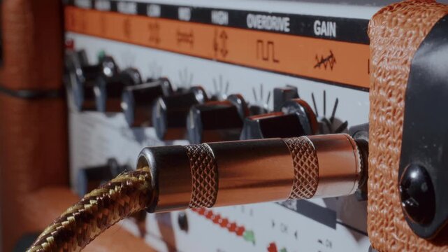 Hand of musician plugging silver audio cable into vintage guitar amplifier input jack panel. Extreme close-up view