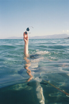 Person Holding Sunglasses While Swimming in Clear Water Near the Shore