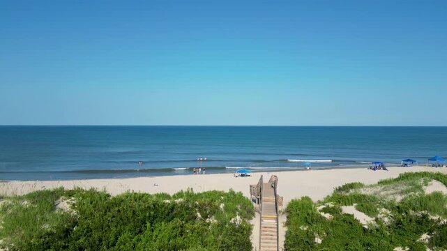 Drone moving down over a wooden boardwalk and the sand dunes from seeing the Atlantic Ocean and Beach in Corolla North Carolina.