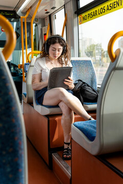 Young woman with vitiligo commuting, listening to music and using a tablet on public transport