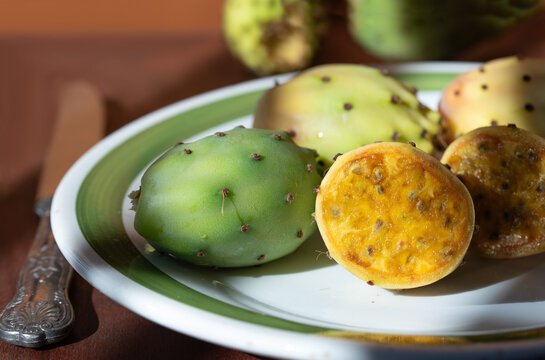 Fresh prickly pears are lying on an old plate in the kitchen. Some of the prickly pears have been cut open.
