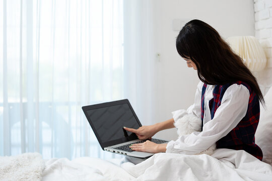 Woman touching laptop screen while working on bed with small white dog, remote work, home, technology, pet companionship, focus, comfort and digital lifestyle