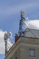 Anteny i urządzenia telekomunikacyjne zamontowane na dachu miejskiego budynku, widoczne na tle błękitnego nieba i białych chmur. © Henryk Guziak