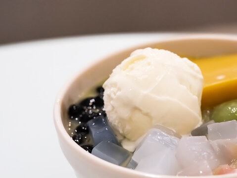 Macro shot focusing on a scoop of creamy vanilla ice cream resting in a bowl of Asian dessert, surrounded by tapioca pearls, jelly cubes, pudding, and mochi.