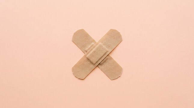 Two beige adhesive bandages crossed to form an X shape on a matching light peach background.