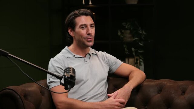 Charming podcast host sitting on a couch speaking into a microphone during a radio show
