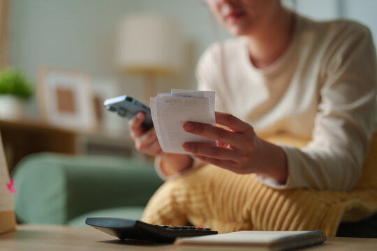 Person reviewing multiple receipts with smartphone and calculator at home, expense tracking, personal budgeting, consumer spending and household money management