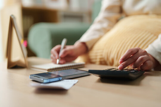 Person using calculator, smartphone and notebook to calculate household expenses at home, budgeting, expense tracking, financial planning and money management