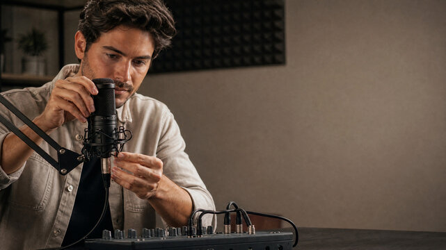Professional male podcaster adjusting microphone in studio, young man recording podcast with audio mixer, content creator at work