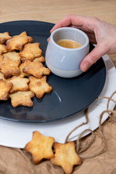 Home cuisine. Shortbread snacks. Female hand holding cappuccino mug with golden crust star cookies served on plate craft paper table.