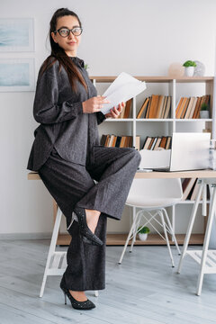 Professional workflow. Office worker. Confident female specialist reviewing business paper at desk with laptop at modern workplace.
