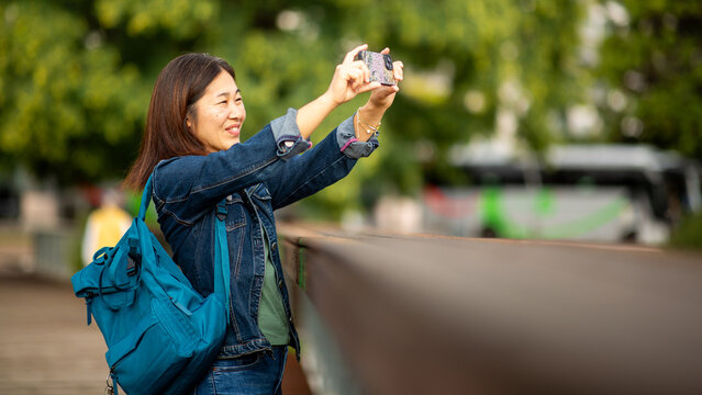 East Asian woman taking smart phone photo on bridge outdoors