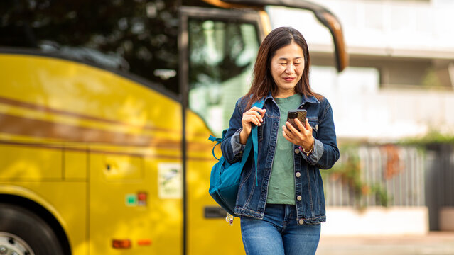 Japanese woman using smart phone while walking near yellow coach bus