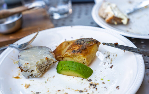 A partially eaten breakfast plate with a piece of buttered bread, a rolled omelet, and a slice of fresh avocado