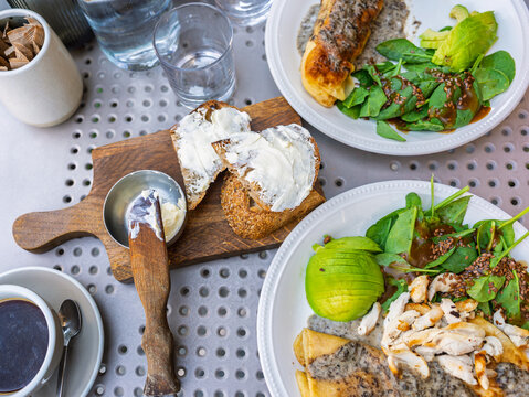 Top view of a healthy brunch with chicken crepes, avocado, spinach salad, and toasted bread with cream cheese on a metal table