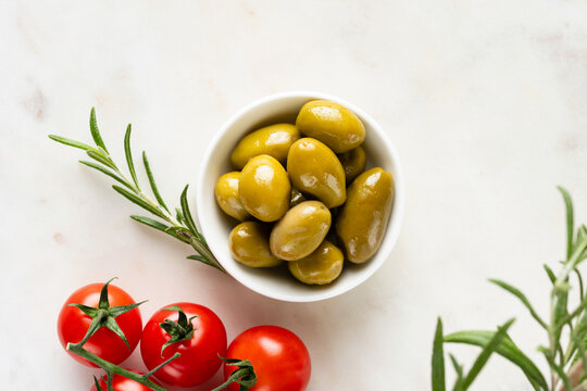 Green whole olives with olive oil in white porcelain bowl, top view