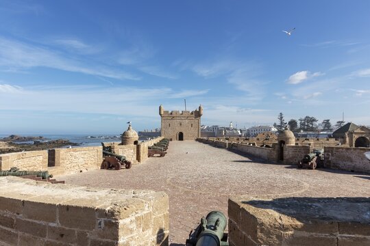 Large stone wall of a fortress with cannons and a wide view of the sea on a clear, sunny day