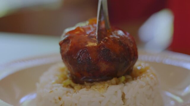 Close up of a knife cutting into a juicy glazed hamburg steak served over white rice. Mouth-watering savory meat juices and sauce flowing out. Delicious gourmet meal shot with selective focus.