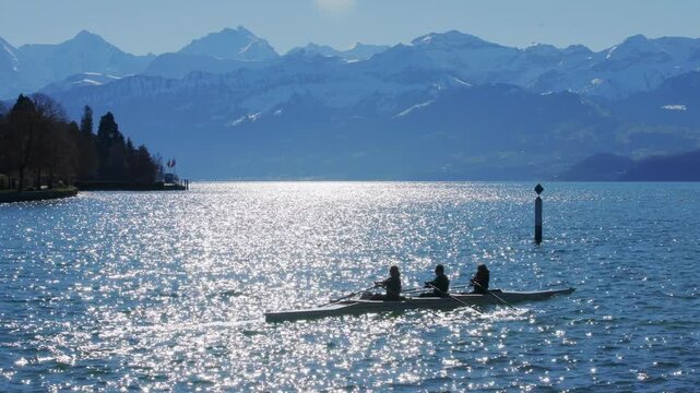 Rowers in rowboat silhouette on Lake Thun with Swiss Alps