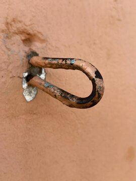 Rusty metal eye hook secured in textured wall with weathered patina during daylight