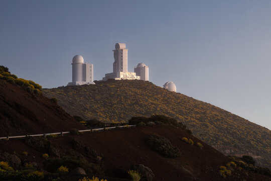 View of Observatorio Astronomico del Teide with white telescope domes situated on a volcanic mountain slope under a clear sky in Izana, Canarias, Spain.