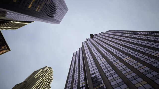 Dramatic low angle view of towering facades, deep vertical convergence and strong composition, moody sky and illuminated windows create cinematic urban energy