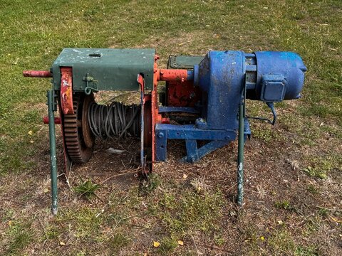 Industrial winch with electric motor and cable, featuring a green and blue color scheme, positioned on grass in an outdoor setting