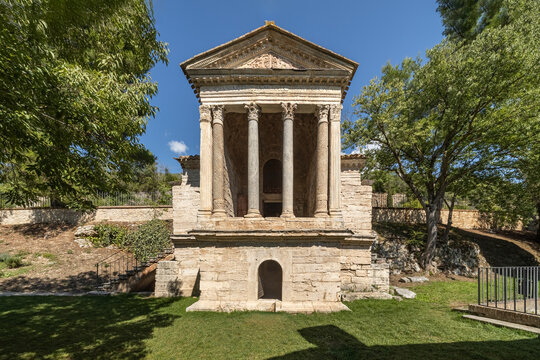 View of the Temple of Clitunno with its ancient stone columns and pediment surrounded by lush trees and green grass in Pissignano, Umbria, Italy.