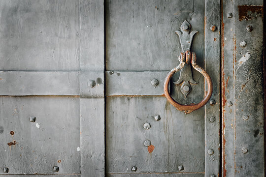 Close-up of an antique weathered metal door with a decorative iron door knocker, rivets, rust and textured surface.