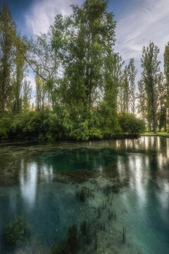 View of the crystal clear turquoise water of Fonti del Clitunno reflecting the surrounding lush trees and greenery in Campello Sul Clitunno, Umbria, Italy.