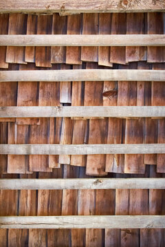 Rustic wooden wall made of weathered shingles and horizontal timber beams, showcasing natural wood grain, warm earthy tones, aged texture and traditional architectural craftsmanship