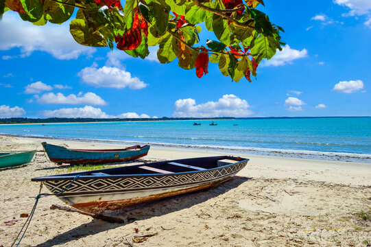 Traditional wooden boat with indigenous patterns on the pristine beach of Coroa Vermelha, Bahia, Brazil. Sunny tropical landscape with turquoise sea and sky.