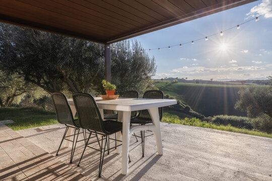 View of a patio with a table and chairs overlooking the rolling hills and olive groves of the Marche countryside in Petriolo, Marche, Italy.