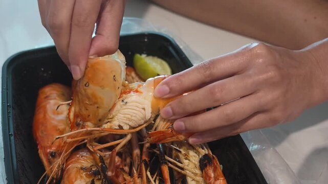 Hands peeling a grilled giant river prawn with lime in a food tray