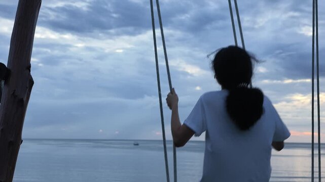 Rear view of a woman relaxing on a swing watching the sea at twilight