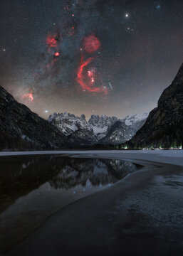 View of Durrensee at night with a starry sky, nebula, and snow-covered mountains reflected in the frozen lake in Toblach, Trentino-Alto Adige, Italy.