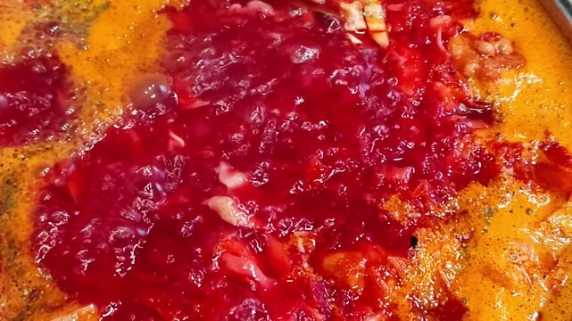 Cooking homemade borscht, red beet soup with cabbage and meat boiling in a stainless steel pot on the stove, bubbling broth with foam, close-up, top view. Traditional Eastern European soup.