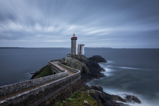 View of Le Phare du Petit Minou lighthouse standing on a rocky cliff connected by a stone bridge over the Atlantic Ocean in Plouzane, France.