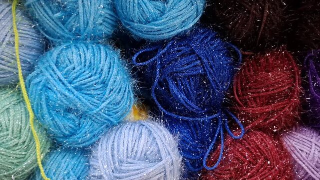 Many colorful yarn balls with lurex thread lie stacked together in a craft store. knitting hobby, needlework supply, textile materials background.