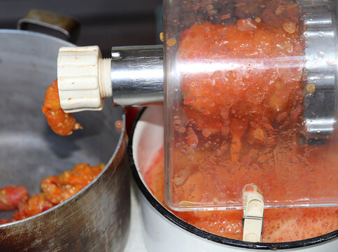 Close-up of fresh tomatoes being processed through a manual food grinder, with crushed tomato pulp collecting in a bowl during homemade sauce preparation.