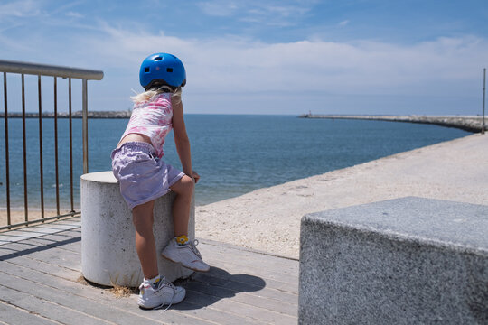 Little Girl Wearing a Blue Helmet Looking at the Sea from a Pier