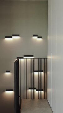 Vertical video. Wall lighting highlights stairs and a black railing inside a contemporary space.