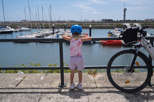 Little Girl Looking at Yachts in the Marina Next to a Bicycle